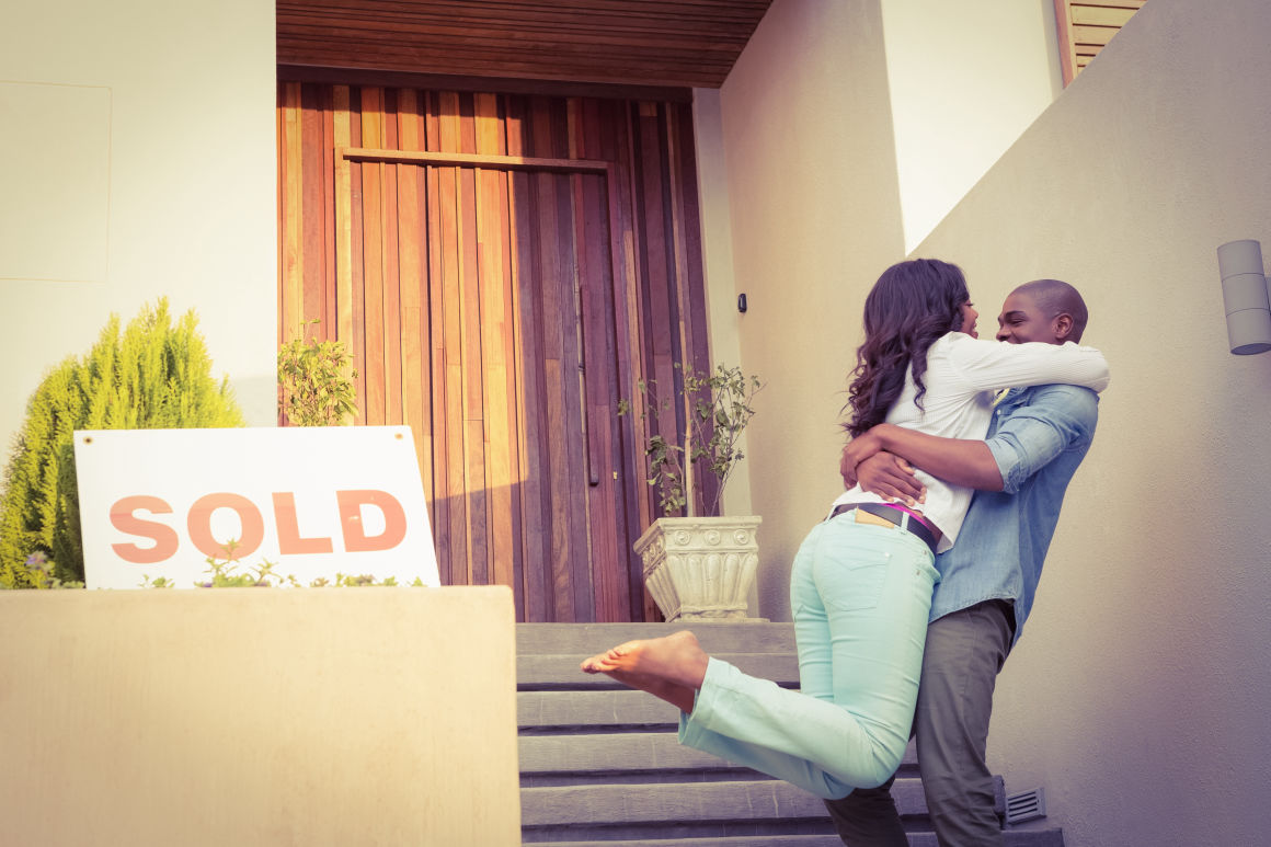 happy couple hugging outside a home with a sold sign